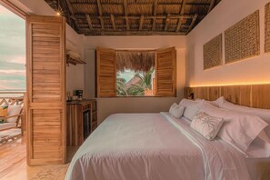 Une chambre avec un lit, des murs en bois, un plafond de chaume, une vue sur des palmiers et un balcon.