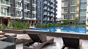 A modern outdoor pool area with wicker lounge chairs, surrounded by a poolside deck and a view of high-rise residential buildings. - 81 Newport Boulevard Across Naia T3 Airport (Pasay)