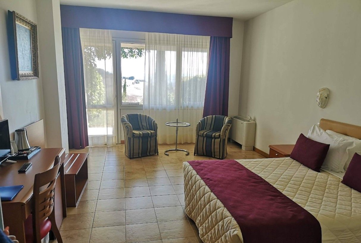 Een hotelkamer met een bed, een bureau, twee stoelen, een tafeltje en een raam met gordijnen.