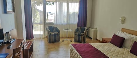 Una camera d'albergo con un letto, una scrivania, due sedie, un tavolino e una finestra con tende.