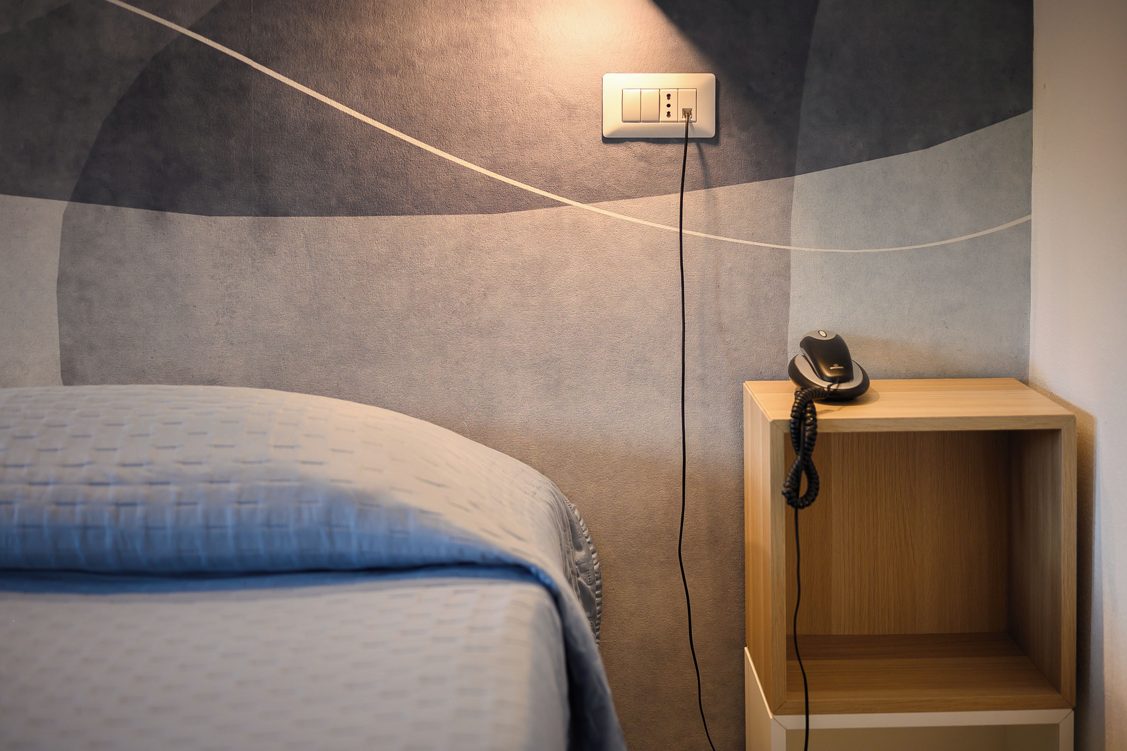 A bedroom with a bed, a bedside table with a telephone, and a wall socket.