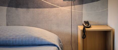 A bedroom with a bed, a bedside table with a telephone, and a wall socket.