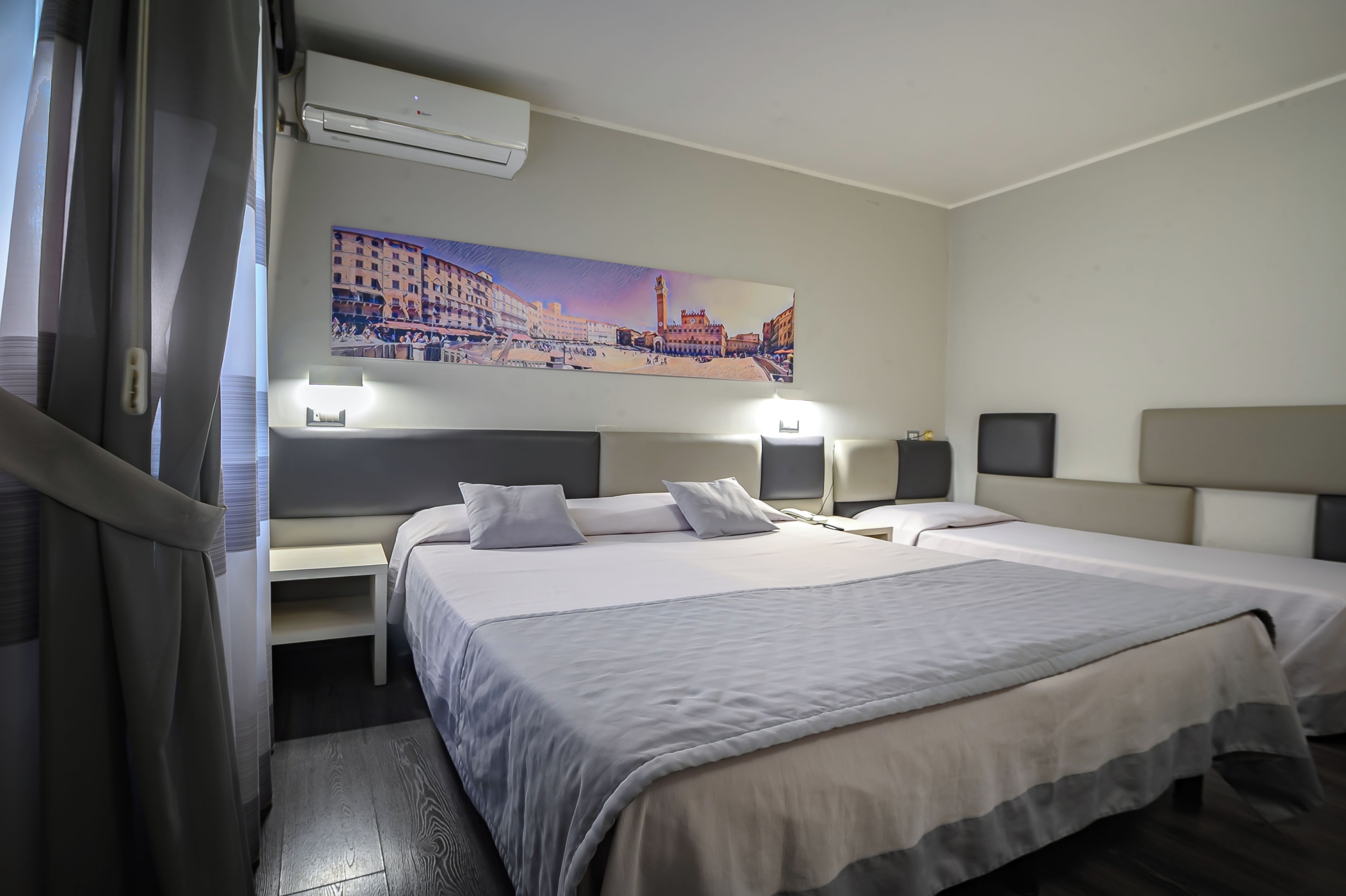 Camera d'albergo con due letti, un quadro raffigurante un panorama urbano, un condizionatore d'aria e abat-jour.