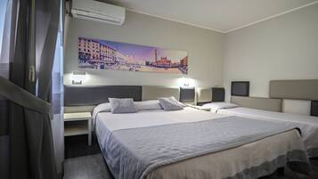 Camera d'albergo con due letti, un quadro raffigurante un panorama urbano, un condizionatore d'aria e abat-jour.