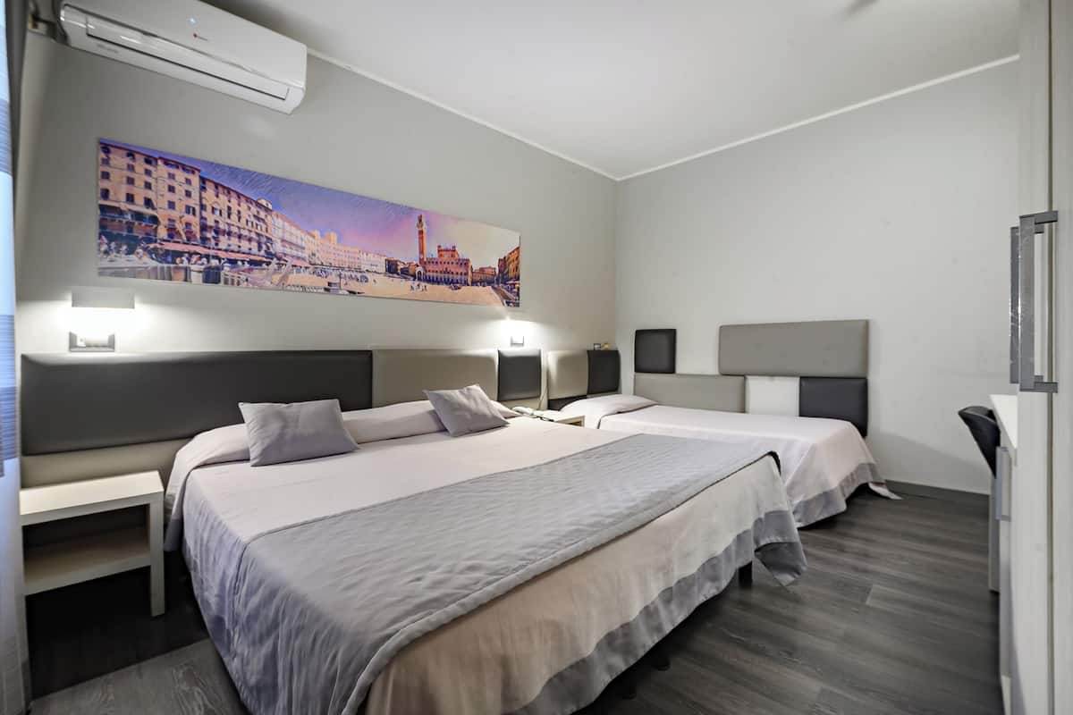 A hotel room with two beds, a large cityscape painting on the wall, and a desk with a chair.