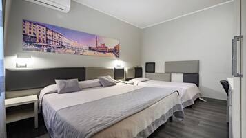 Camera d'albergo con due letti, un quadro di un panorama cittadino e una scrivania con una sedia.