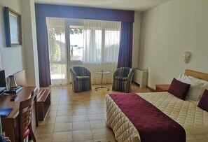 Een hotelkamer met een bed, twee fauteuils, een kleine tafel, een bureau met een computer en een raam met gordijnen.