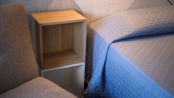 A bedroom with a wooden bedside table, a blue quilted bedspread, and a grey upholstered chair.