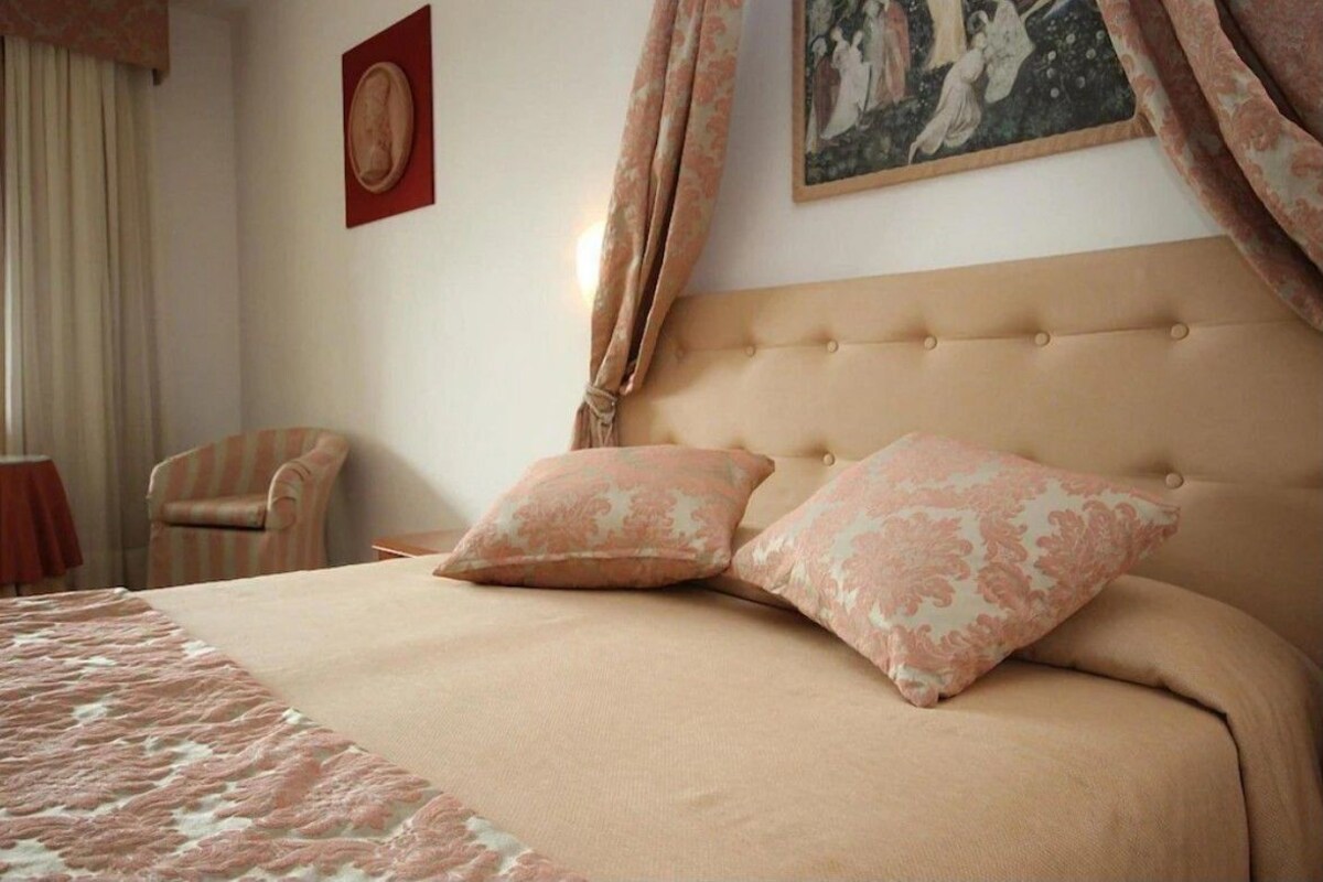 Una cama bien tendida con dos almohadas a juego, un sillón a rayas y un cuadro en la pared.