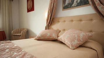 A neatly made bed with two matching pillows, a striped armchair, and a painting on the wall.