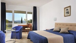 A hotel room with a large bed, a desk, and a chair. There is a window with a view of the countryside. - Relax Hotel Acquaviva - Tuscany Hills (Casole d'Elsa)