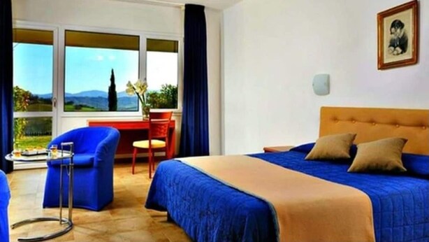 A hotel room with a bed, a desk, a chair, and a view of the outdoors. - Relax Hotel Acquaviva - Tuscany Hills (Casole d'Elsa)