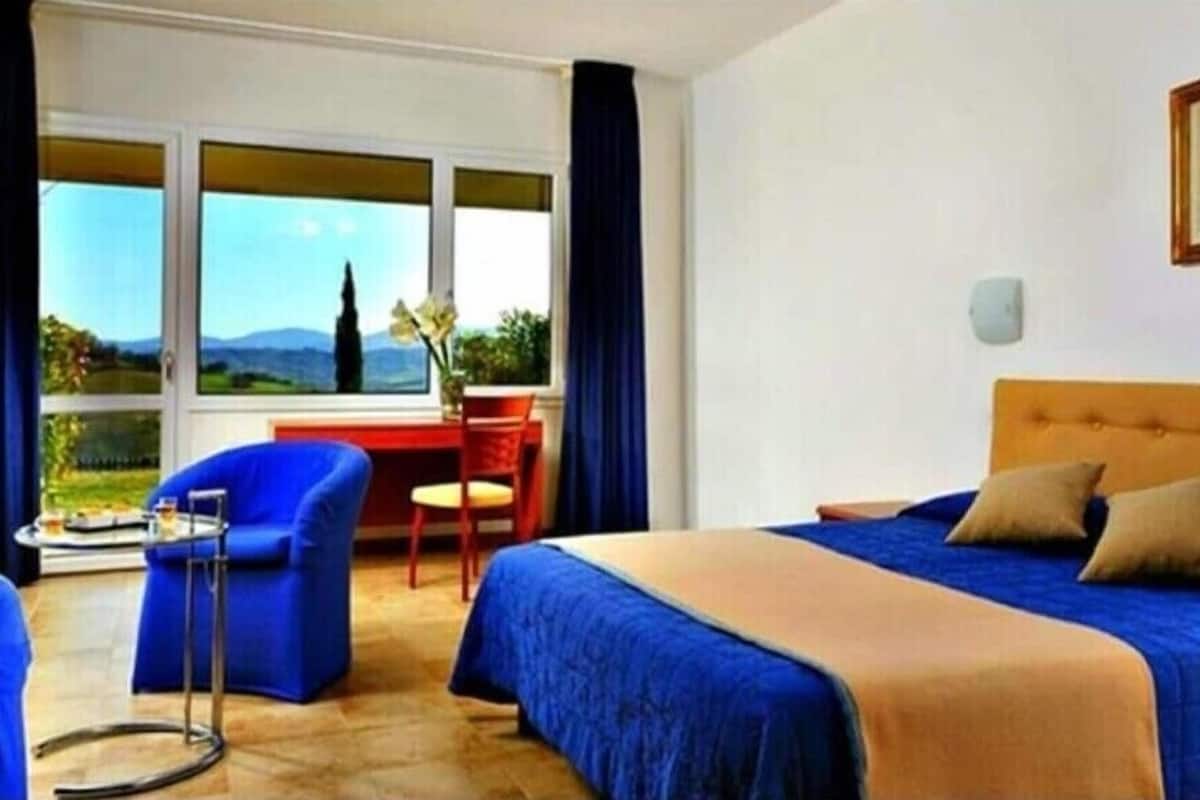 A hotel room with a bed, a desk, a chair, and a view of the outdoors.