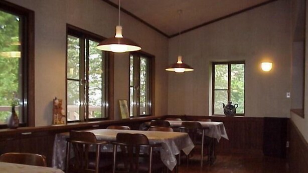 A dining area with tables and chairs, large windows, and hanging pendant lights. - Pension Mori no Symphony (Shinano)
