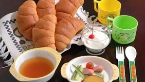 A table with a plate of food, a bowl of soup, a cup of tea, a glass of milk with a cherry, and a green mug. - Pension Mori no Symphony (Shinano)