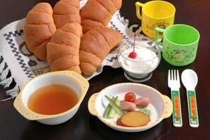 Une table avec une assiette de nourriture, un bol de soupe, une tasse de thé, un verre de lait avec une cerise et une tasse verte.