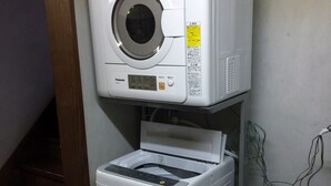 A stacked washer and dryer unit with a control panel, a power cord, and a small shelf with items. - Pension Mori no Symphony (Shinano)
