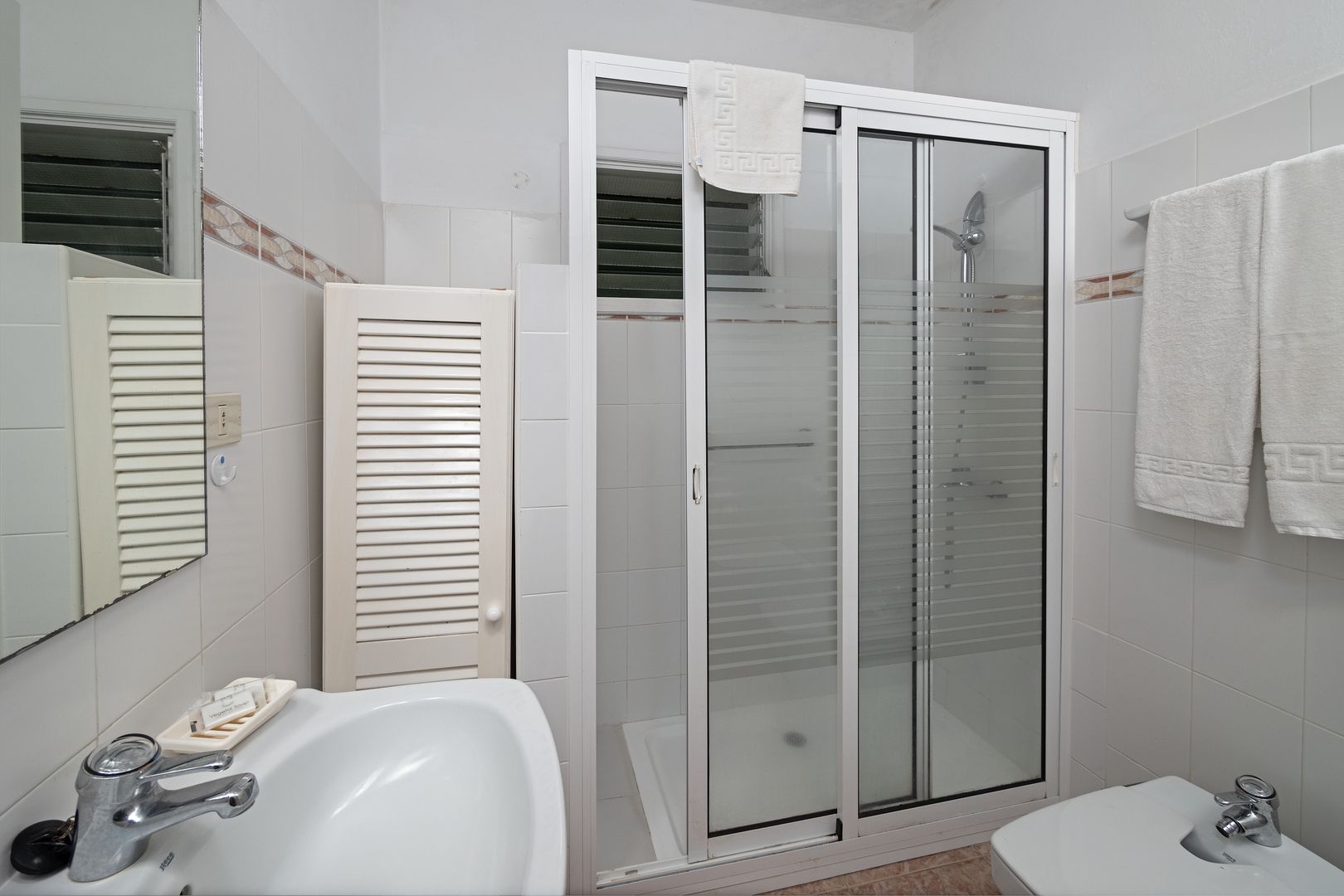 Casa de banho com cabine de duche em vidro, lavatório branco e sanita.
