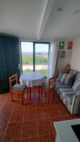 Una habitación con una mesa redonda, dos sillas, un sofá, vista al mar y un extintor.