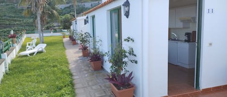 A white building with a tiled roof, a kitchen area, and a pathway lined with potted plants.