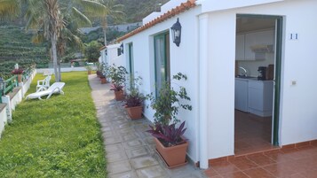 Un edificio blanco con techo de tejas, una zona de cocina y un sendero bordeado de macetas.