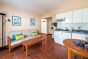 Un espacio habitable pequeño con sofá, mesa de comedor, zona de cocina y una lámpara de pie.