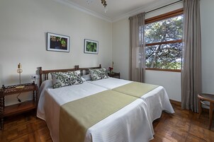 Una cama doble con dos almohadas, una mesita de noche con lámpara y una ventana con cortinas.