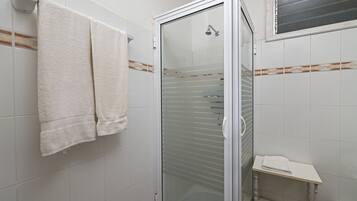 A bathroom with a glass-enclosed shower, white tiles, a towel rack, and a small shelf.