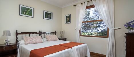 A bedroom with a wooden bed, two bedside tables, a nightstand, a window with curtains, and framed pictures on the wall.