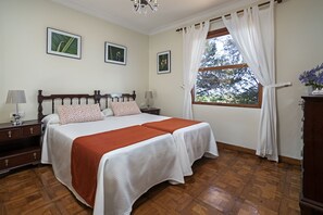 A bedroom with a wooden bed, two bedside tables, a nightstand, a window with curtains, and framed pictures on the wall. - Sabinas & Terrazas Malpaís (Icod de los Vinos)