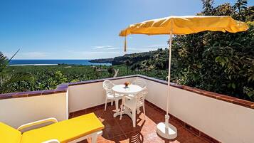 A balcony with a table and chairs, a yellow umbrella, and a view of the ocean.