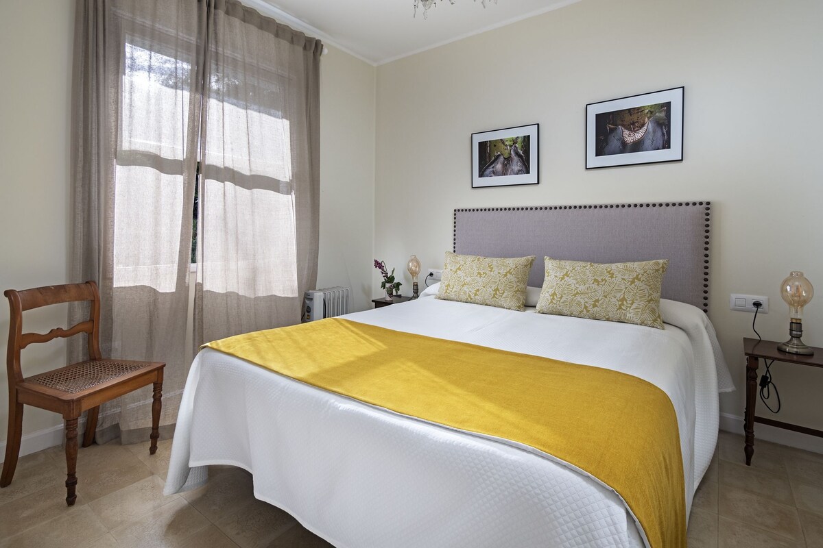 A bedroom with a bed, a chair, a bedside table, a lamp, and two framed pictures on the wall.