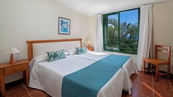 Habitación de hotel con una cama grande, un escritorio, una silla, una ventana con vista a palmeras y un cuadro en la pared.