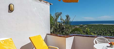 Un balcón con sillas amarillas y una mesa, con vistas panorámicas al océano y vegetación.