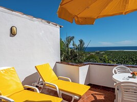 Un balcón con sillas amarillas y una mesa, con vistas panorámicas al océano y vegetación.