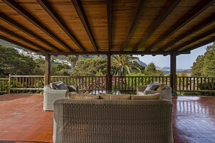 Un área de estar al aire libre techada con mobiliario de mimbre y vistas al paisaje.