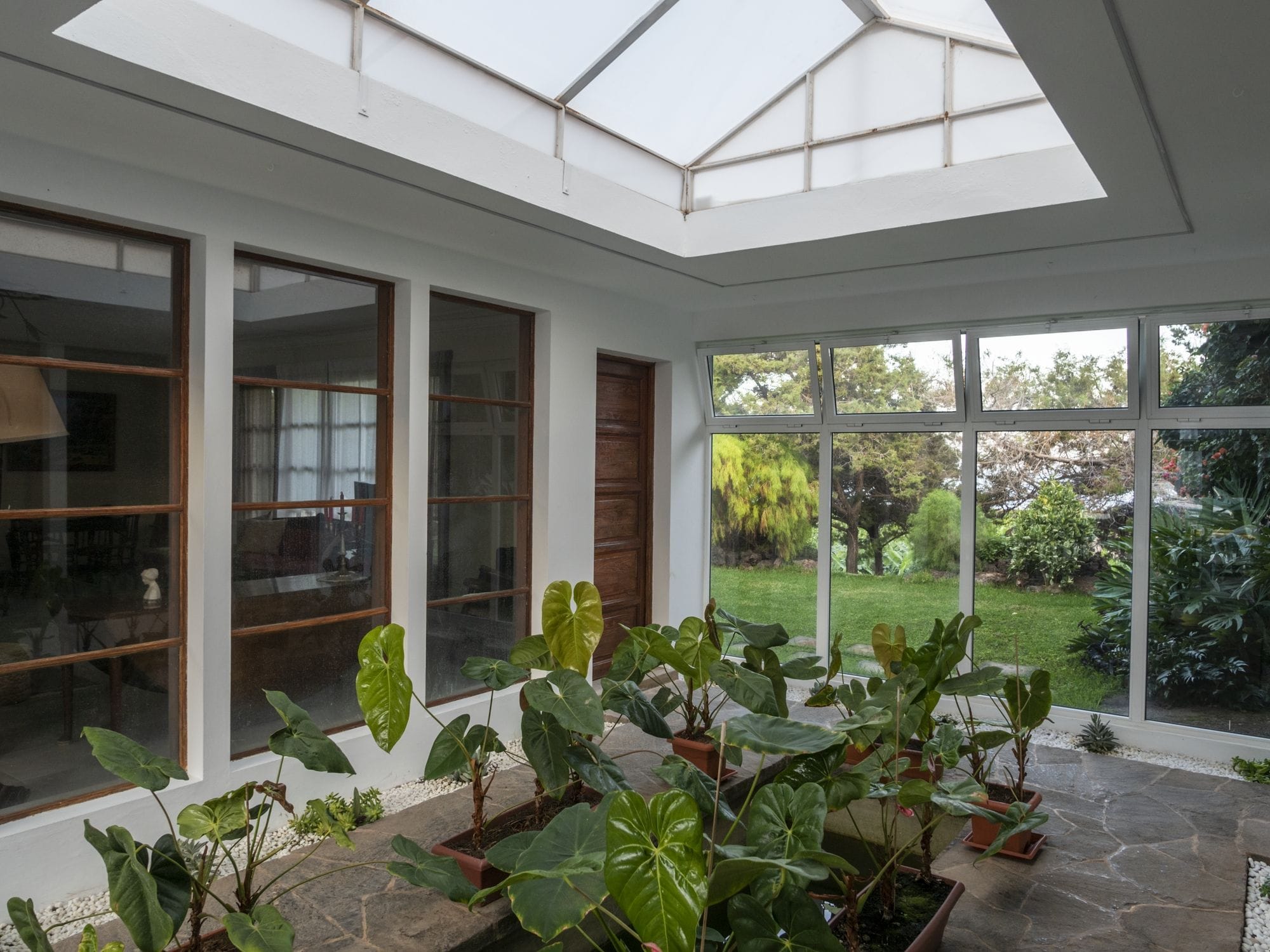 Una sala de estar con ventanales amplios, plantas en macetas y vistas a un jardín.