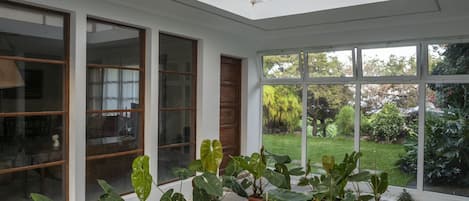 Una sala de estar con ventanales amplios, plantas en macetas y vistas a un jardín.