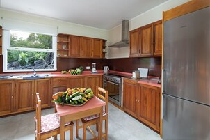 Cocina con armarios de madera, refrigerador de acero inoxidable, estufa y ventana con vista a follaje.