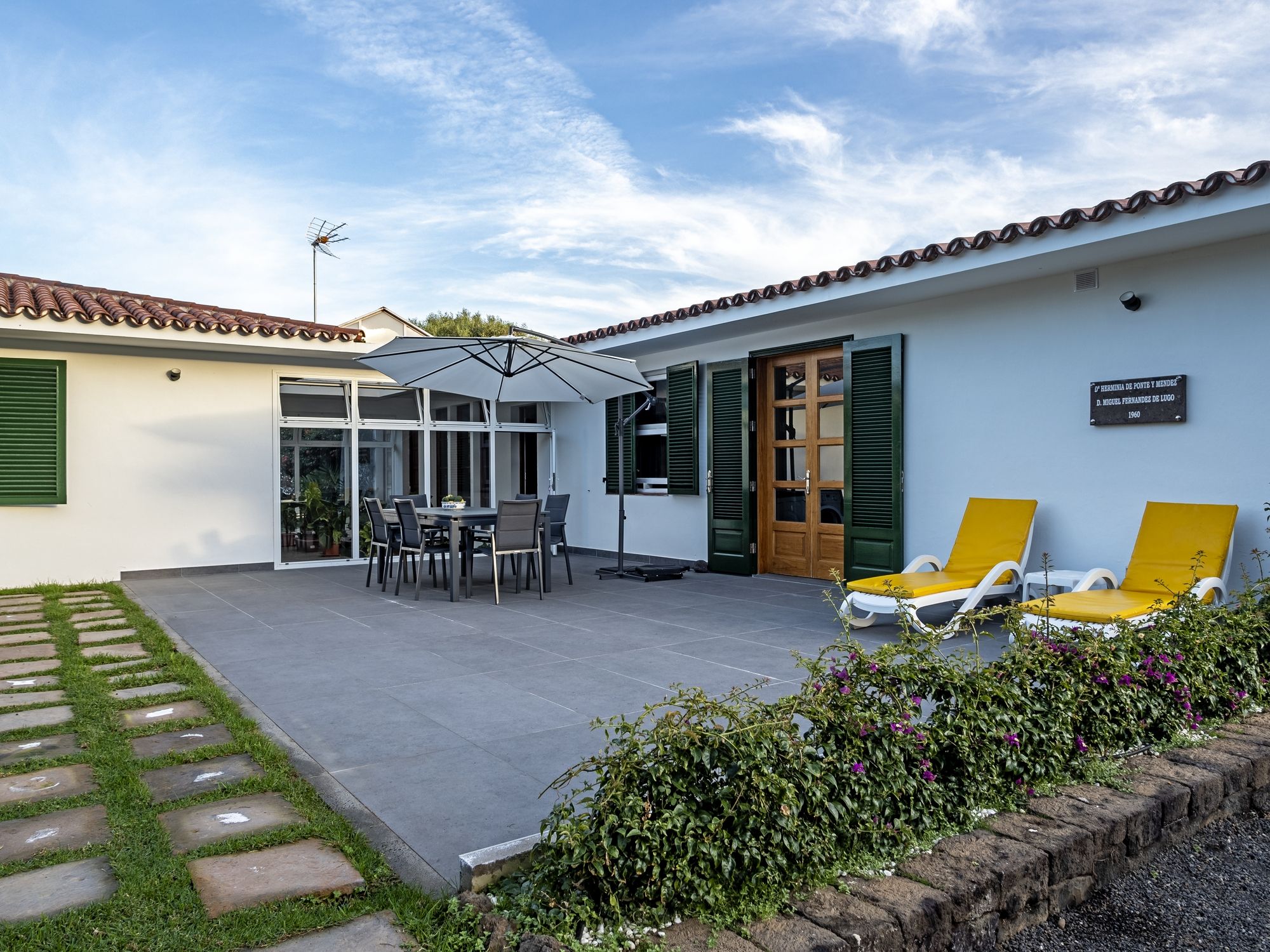 A patio with a table and chairs, a covered area, and two sun loungers.