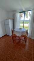 Un comedor con mesa y sillas, un refrigerador y vista al océano.