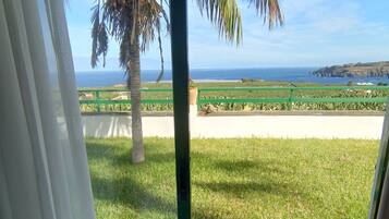A room with a view of the ocean, a palm tree, and a table with a fruit bowl.