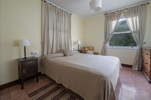 A bedroom with a bed, two bedside tables with lamps, a dresser, a window with curtains, and a view of greenery outside. - Sabinas & Terrazas Malpaís (Icod de los Vinos)
