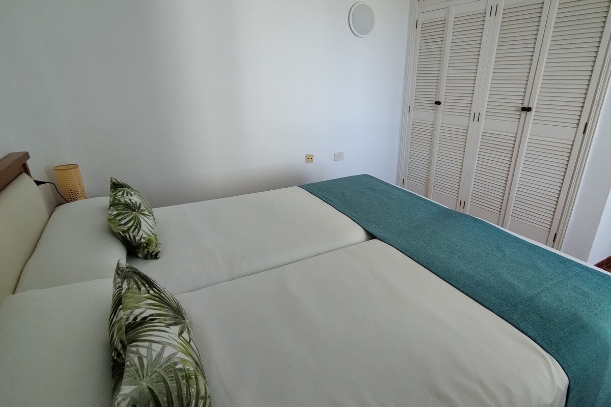 A bed with a teal blanket, a wooden headboard, and two green pillows.