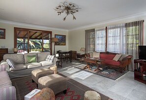 A spacious living room with a sofa, ottoman, and a red sofa, a dining area with a table and chairs, and a television on a wooden stand. - Sabinas & Terrazas Malpaís (Icod de los Vinos)