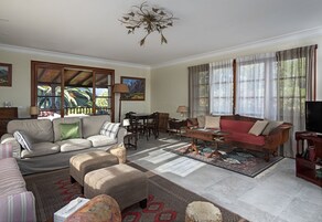 Un salón amplio con sofá, reposapiés y un sofá rojo, un comedor con mesa y sillas, y un televisor sobre un mueble de madera.