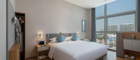 A modern bedroom with a large bed, bedside tables, a wardrobe, and a city view.