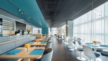 A modern restaurant with a long counter, seating area, and large windows.