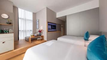 Et moderne hotelværelse med to senge, et skrivebord med computer, et fjernsyn og et vindue med let gardin.