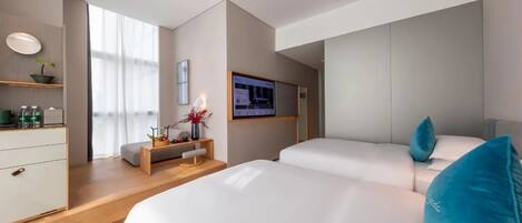 Une chambre d’hôtel moderne avec deux lits, un bureau avec un ordinateur, une télévision et une fenêtre avec des rideaux légers.
